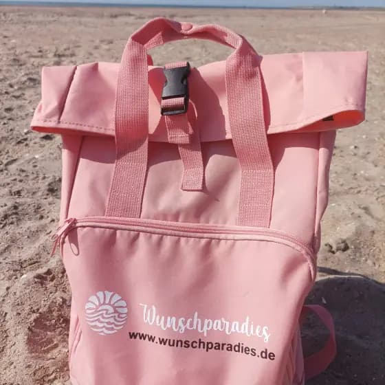 Rosa Rucksack mit Wunschparadies-Druck am Strand